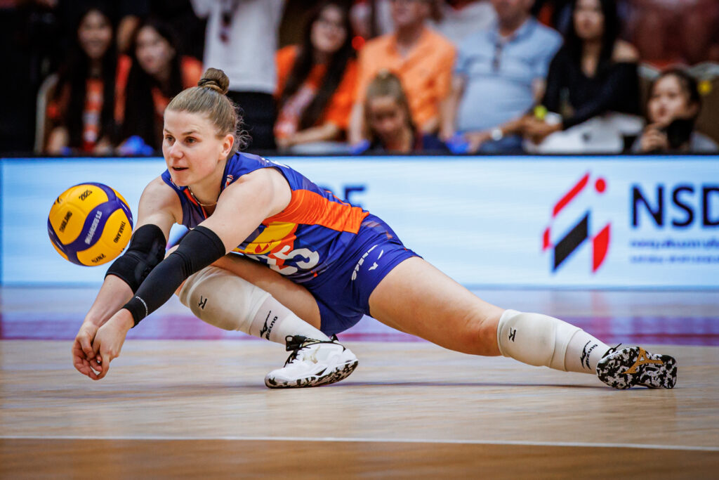 Florien Reesink duikt naar de grond om een volleybal te redden tijdens een wedstrijd, volledig gefocust op de bal.