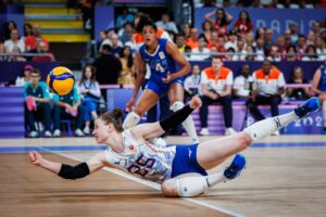Florien Reesink duikt naar de grond om een volleybal te redden tijdens een wedstrijd, volledig gefocust op de bal.